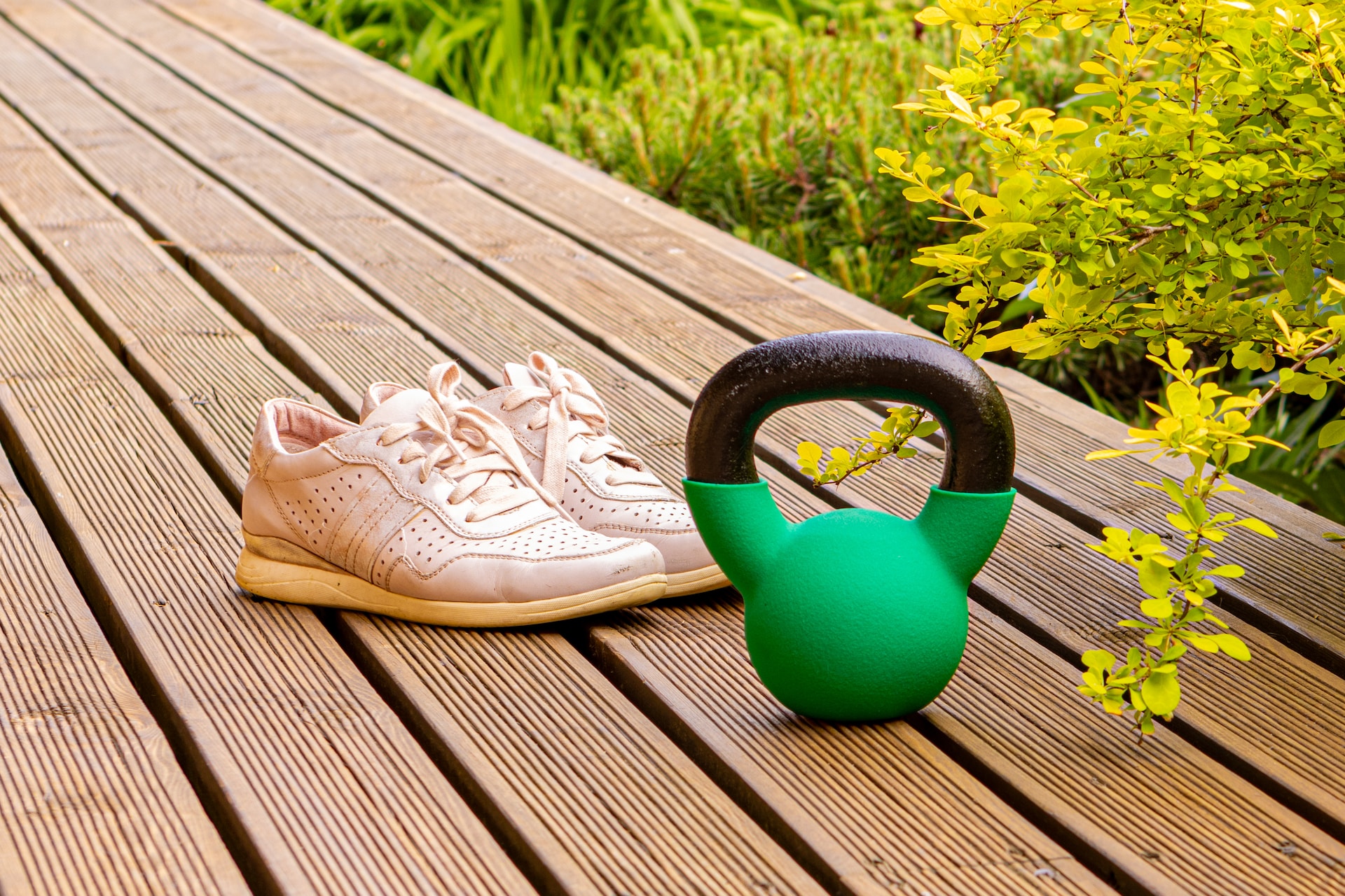 trainers and a kettlebell on decking with shrubbery behind